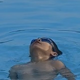 Amir floating on his back in the pool, wearing swim goggles